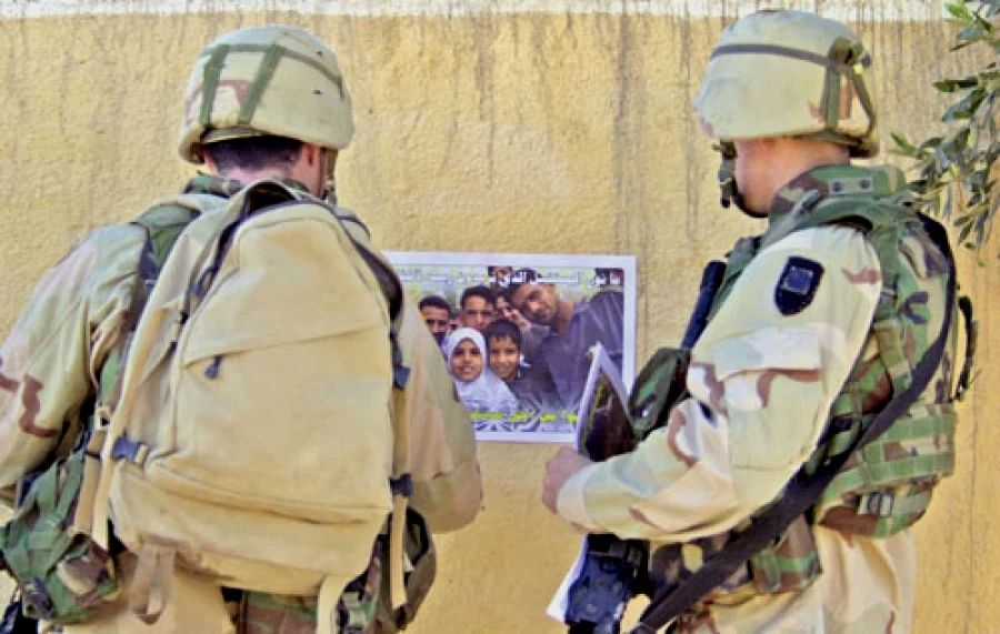 2005年，两名在拉马迪的陆军503步兵团1营的士兵在检视一张街头海报。从扣具和拉链头推测左边这名士兵使用的是BHI的产品