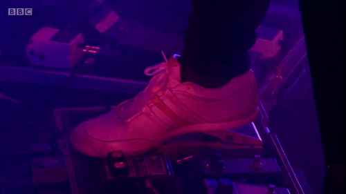 一张图片：Jonny 在 2017年 Glastobury 音乐节上，Radiohead 用脚调整 DOD 440。他的 Demeter TRM-1 Tremulator 能被清楚看见。这双鞋是阿迪达斯 Y3 boxing trainer。