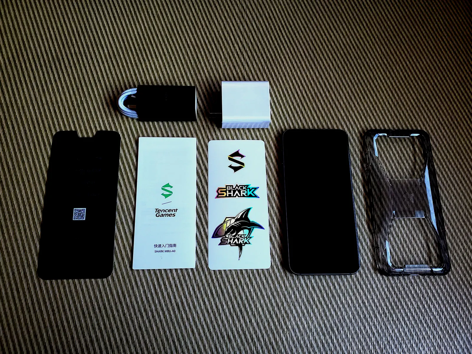 一部已经贴膜的腾讯黑鲨游戏手机3 Pro、一个透明手机壳、一张黑鲨贴纸、一个卡针、一个65W充电器以及一根Type-C充电线